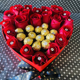 Heart-shaped box of red roses with gold-wrapped chocolates and a ribbon bow