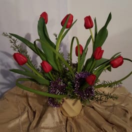 Red tulips arranged in a beige vase with purple filler flowers