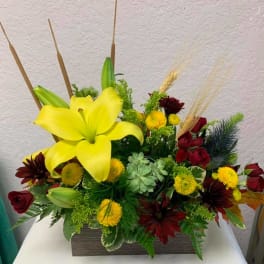 Yellow lilies and red roses in a rectangular vase with mixed accents