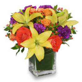 Bouquet of yellow lilies, orange roses, and purple flowers in a glass vase