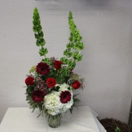 Tall floral arrangement with red roses, burgundy daisies, and white hydrangeas in a glass vase
