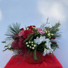 Red roses and white flowers in a red container with pine accents