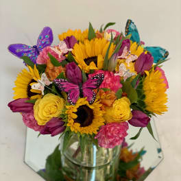 Bouquet of sunflowers, tulips, and roses in a glass vase with butterfly picks