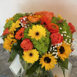 Bouquet of yellow daisies, orange roses, and green hydrangeas in a glass vase