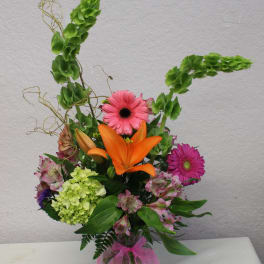 Mixed bouquet with orange lily, pink gerbera daisies, and green hydrangea in a glass vase