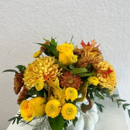 Yellow roses and chrysanthemums arranged in a white vase with autumn leaves