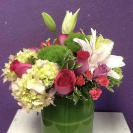 Bouquet of pink roses, white lilies, and pale hydrangeas in a green vase