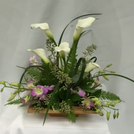 White calla lilies and purple orchids in a low wooden container