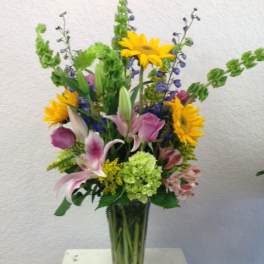 Tall mixed bouquet in a glass vase with sunflowers, lilies, and roses