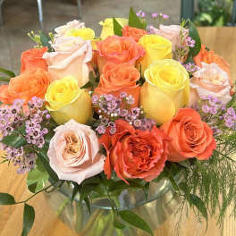 Mixed roses in orange, yellow, and blush arranged in a glass vase