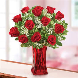 Red roses arranged in a red glass vase with white filler flowers