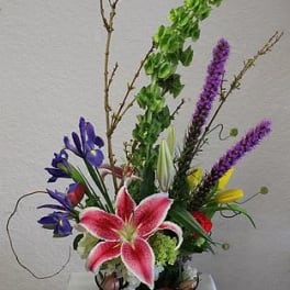 Tall mixed flower arrangement with a pink lily in a glass bowl