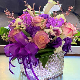 Purple and pink floral arrangement in a clear textured cube vase