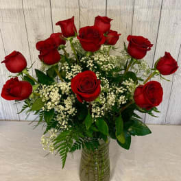 Red roses arranged in a clear glass vase with white filler flowers
