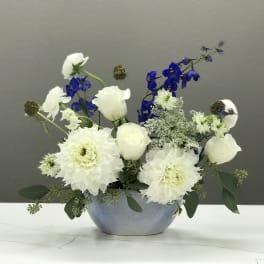 White and blue floral arrangement in a round blue vase