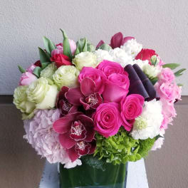 Mixed bouquet of pink, white, and green flowers in a square glass vase