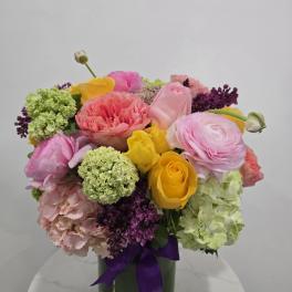 Colorful bouquet of roses and ranunculus in a glass vase with a purple ribbon