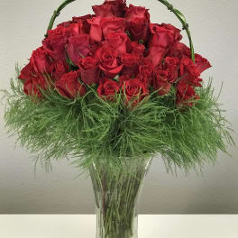 Red roses arranged in a clear glass vase with a green handle