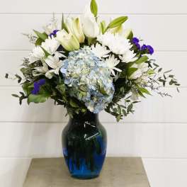 White lilies and daisies with blue hydrangea in a blue vase