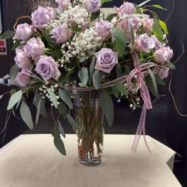 Lavender roses in a clear glass vase with baby's breath and ribbon