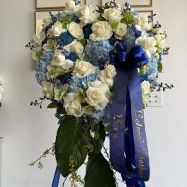 Heart-shaped standing wreath of white roses and blue hydrangeas with blue ribbon on an easel