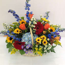 Colorful mixed flower basket with roses, gerberas, sunflowers, and blue delphinium