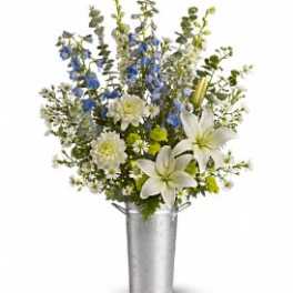 Tall arrangement of white lilies, mums, blue delphinium and small daisies in a silver metal bucket.