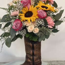 Bouquet of sunflowers, pink roses, and carnations in a cowboy boot vase