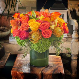 Bright bouquet of orange, yellow, and pink flowers in a green vase
