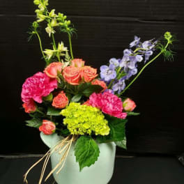 Colorful mixed bouquet in a pale vase with pink, coral, and lavender blooms
