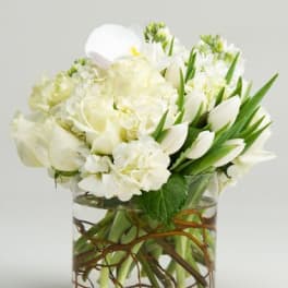 White flowers arranged in a clear glass vase with twisted branches