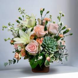 Arrangement of pale pink roses, white lilies, and a succulent in a brown vase