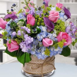 Pink roses and purple calla lilies in a glass vase with blue flowers