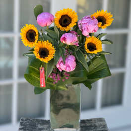 Sunflowers and pink peonies arranged in a tall glass vase