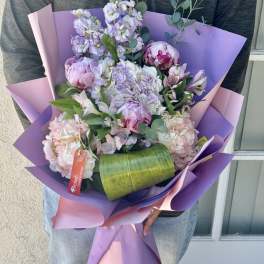 Handheld bouquet of pastel flowers wrapped in purple and pink paper