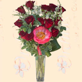 Bouquet of red roses and a pink peony in a tall glass vase