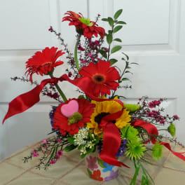 Bright mixed flower arrangement with red gerbera daisies and ribbon in a decorated vase