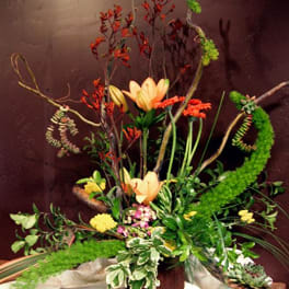 Tall floral arrangement with peach lilies and red-orange blooms