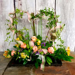 Floral arrangement with peach roses and yellow blooms on a decorative branch frame