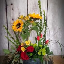 Mixed floral arrangement with sunflowers, red roses, and tulips in a black container