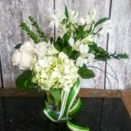 White floral arrangement in a glass vase with ribbon accents