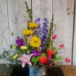 Mixed bouquet in a metal container with sunflowers, lilies, roses, and tulips