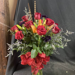 Red roses and orange lilies in a glass vase with a red ribbon