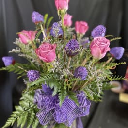 Pink roses and purple flowers in a glass vase with a purple ribbon