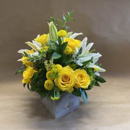 Yellow roses and white lilies arranged in a square vase