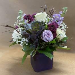 Purple and white floral arrangement in a dark square vase