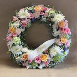 Pastel floral wreath with roses, daisies, and a white ribbon