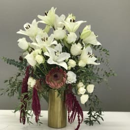 White lilies and roses arranged in a gold vase with burgundy hanging accents.