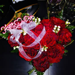 Heart-shaped bouquet of red roses with a pink ribbon and "Happy Anniversary" topper