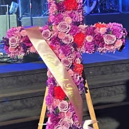 Cross-shaped floral tribute with pink and purple flowers on an easel